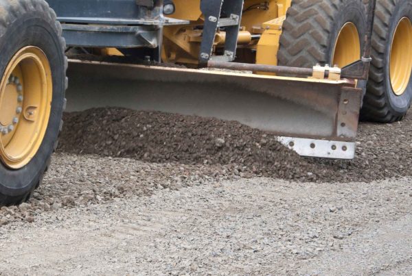 Close-up of a grader grading a driveway sub-base with aggregate gravel.