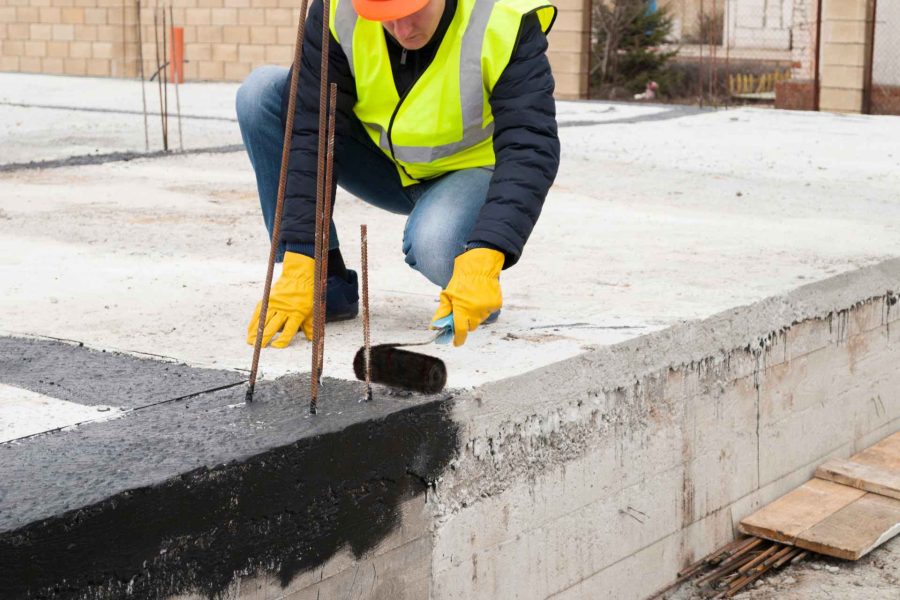 Worker applying liquid waterproofing on the base of the foundation.