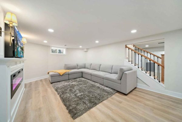 Modern basement living room with a couch, television, fireplace, and a sliding basement window letting in natural light.